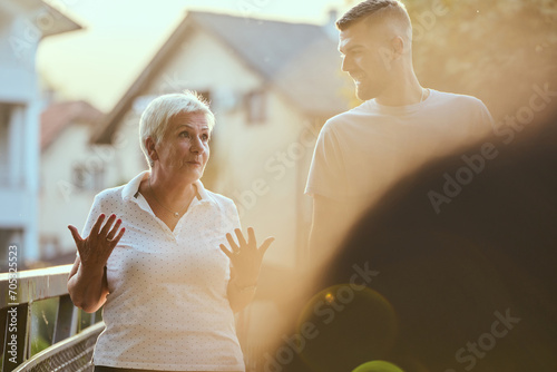 A handsome man and an older woman share a serene walk in nature, crossing a beautiful bridge against the backdrop of a stunning sunset, embodying the concept of a healthy and vibrant intergenerational