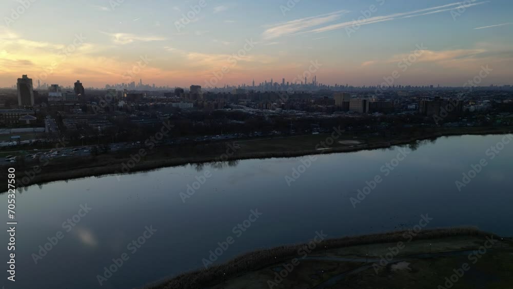 nyc skyline at sunset (aerial drone shot from far away distance in queens) corona flushing meadows park with meadow lake in foreground (setting sun, glow, golden hour) flying up, rising shot nyc skyline at sunset (aerial drone shot from far away distance in queens) corona flushing meadows park with meadow lake in foreground (setting sun, glow, golden hour) flying up, rising shot