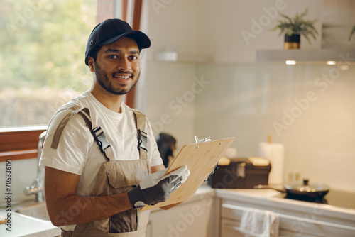 Portrait of young smiling repairman standing with clipboard in kitchen at home photo