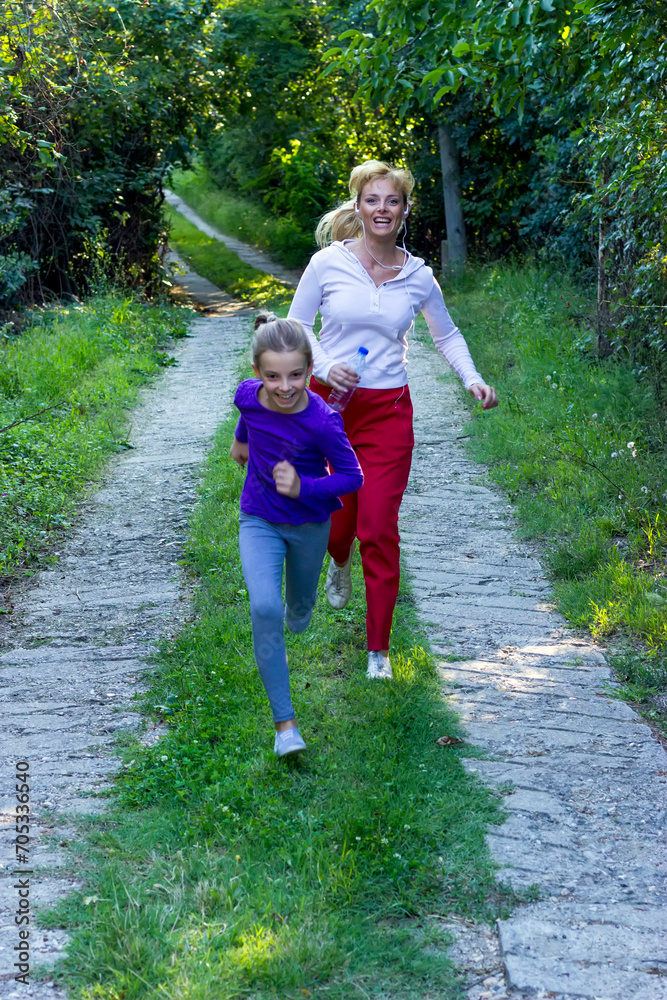 Attractive blonde mother and her cute little daughter running in the public park. Who is faster Attractive blonde mother and her cute little daughter running in the public park. Who is faster