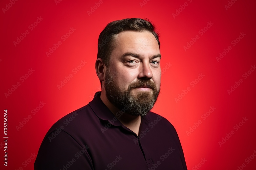 Portrait of a bearded man in a dark purple shirt on a red background.