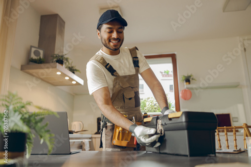 Smiling professional handyman standing on home kitchen and open his tool bag photo