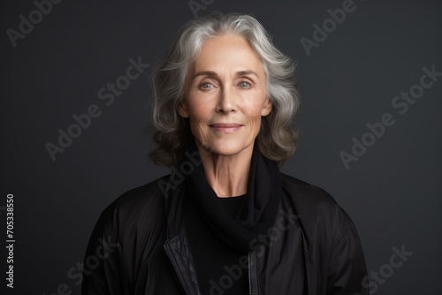 Portrait of a smiling senior woman in black jacket, isolated on grey background