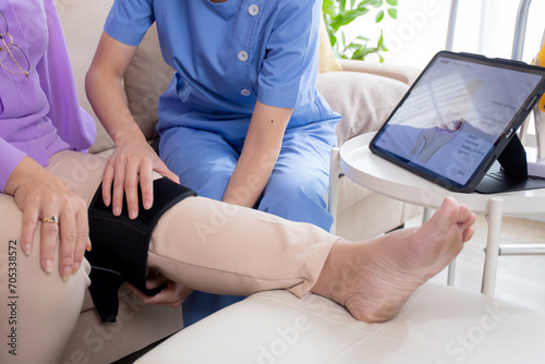 Caregiver or nurse helping check tendon and arthritis of knee or leg for diagnostic and rehabilitation while explaining senior woman with tablet living room at home  caretaker or physiotherapist.