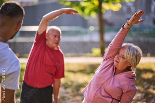 A group of seniors follows a trainer, engaging in outdoor exercises in the park, as they collectively strive to maintain vitality and well-being, embracing an active and health-conscious lifestyle in © .shock