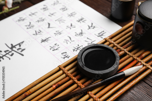 Ink, brush and paper sheet with Asian hieroglyphs on wooden table, closeup. International Haiku Poetry Day