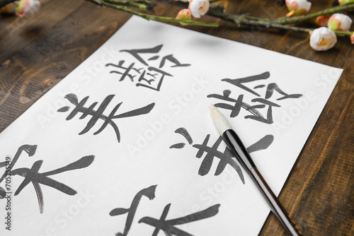 Paper sheet with Asian hieroglyphs and brush on wooden table, closeup. International Haiku Poetry Day #705355149