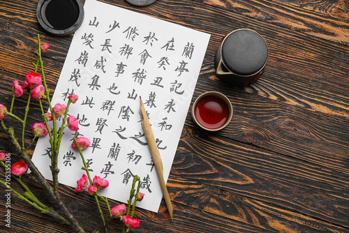 Bild auf Leinwand Paper sheet with Asian hieroglyphs, nib pen, ink, cup of tea and blooming branch on wooden background