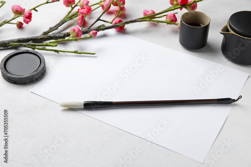 Composition with blank sheet of paper, ink, brush, cup of tea and blooming branch on light background. International Haiku Poetry Day