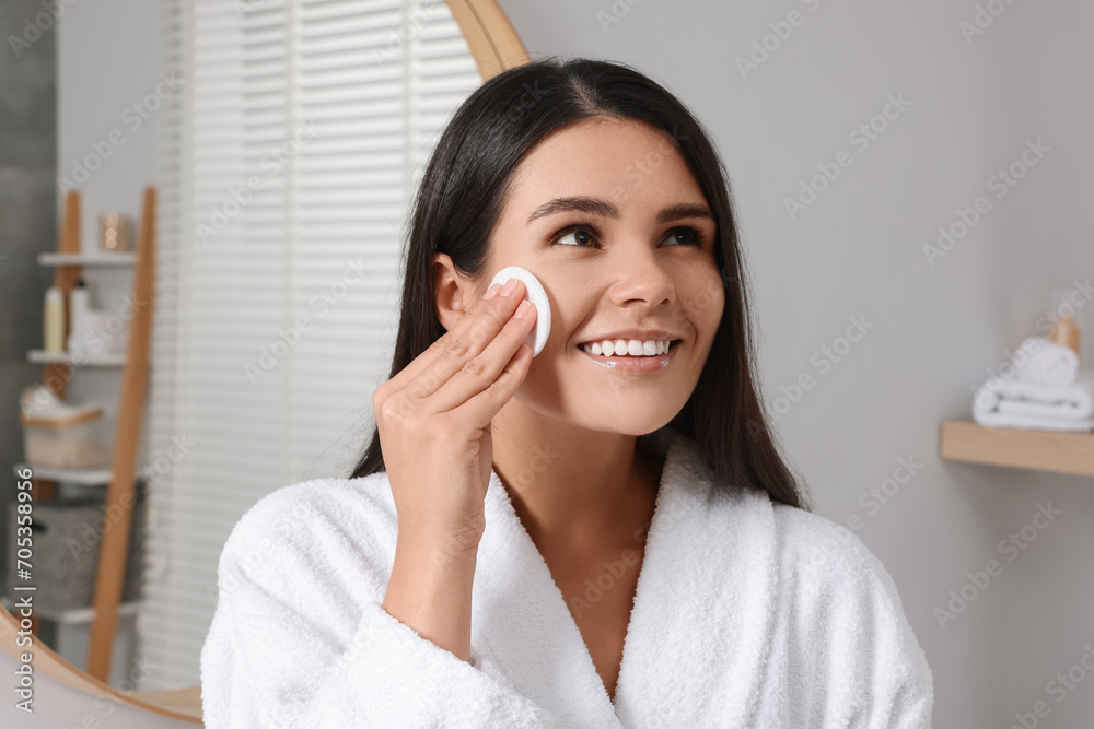 Young woman cleaning her face with cotton pad in bathroom Young woman cleaning her face with cotton pad in bathroom