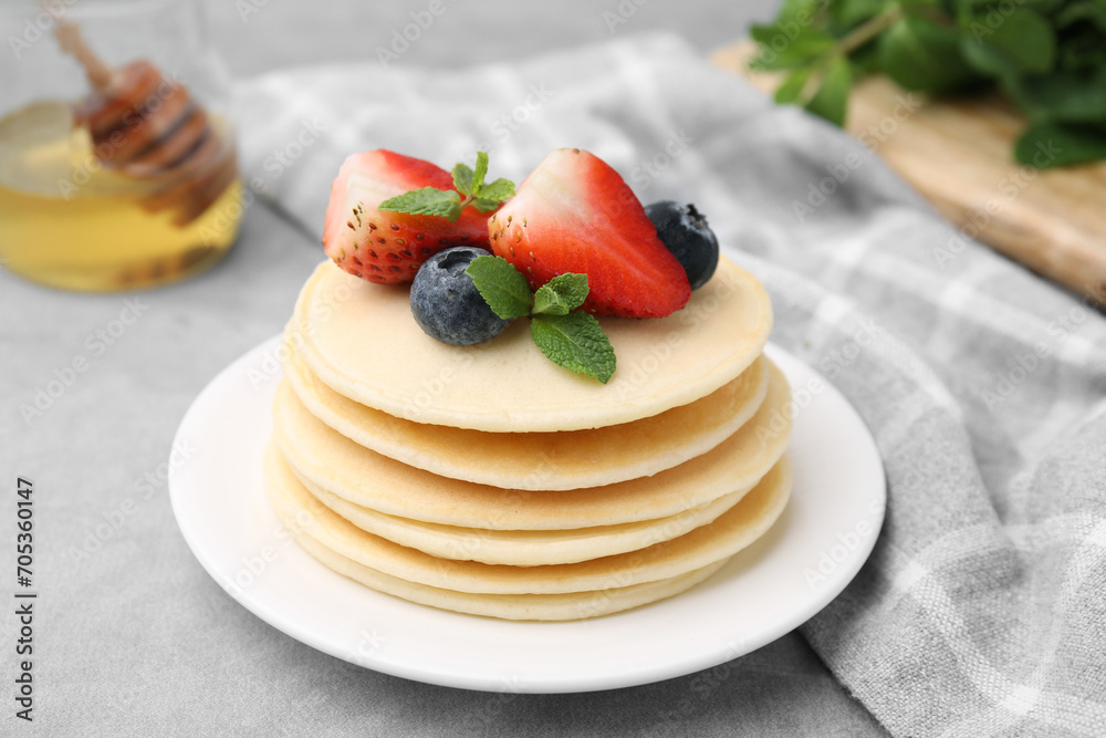 Stack of tasty pancakes with fresh berries and mint on light grey table, closeup Stack of tasty pancakes with fresh berries and mint on light grey table, closeup