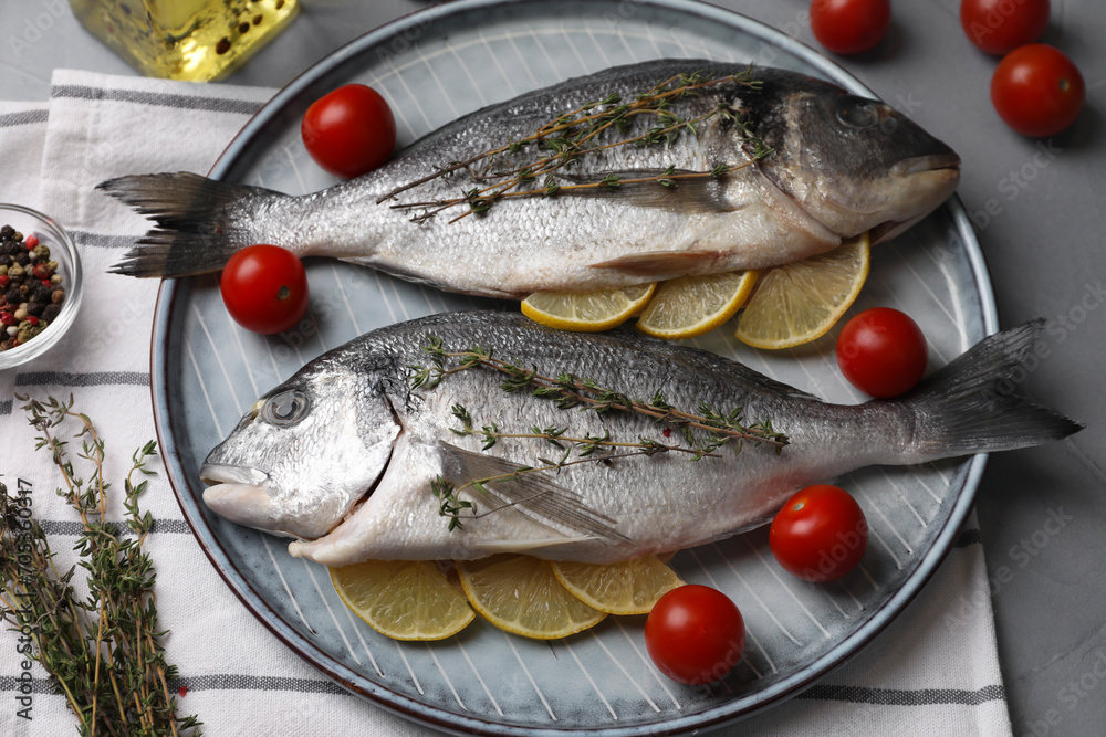Raw dorado fish with thyme, lemon slices and tomatoes on table, closeup