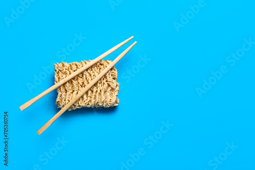 Raw instant noodles and wooden chopsticks on blue background