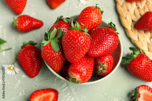 Bowl of fresh strawberries with leaves and chamomile flower on grey background