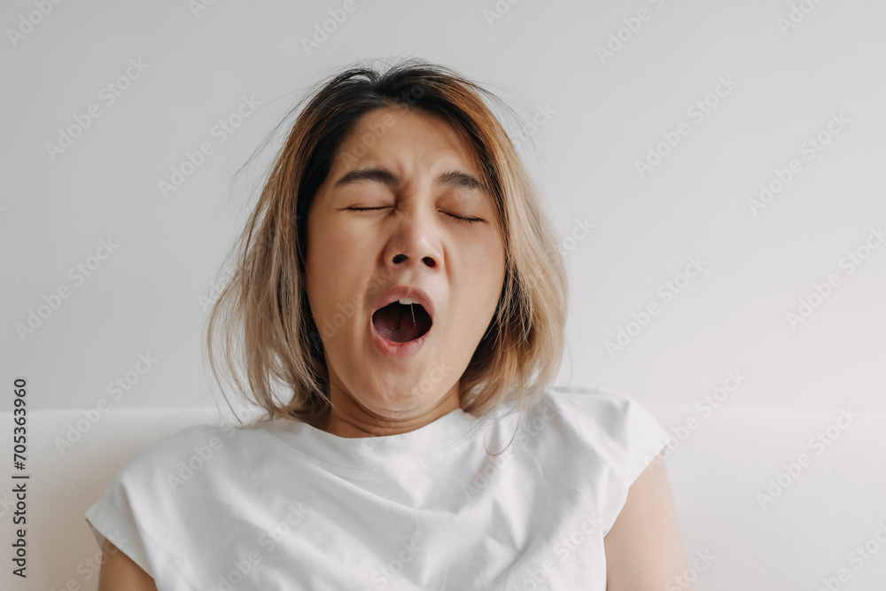 Sleepy face Asian woman yawning and rubbing her eyes in white t-shirt sits on the sofa. Sleepy face Asian woman yawning and rubbing her eyes in white t-shirt sits on the sofa.
