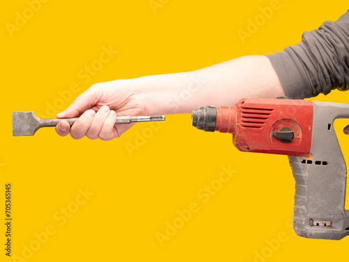 Worker attaches a chisel to an impact drill against a vibrant yellow backdrop. No face, concept, copy space. 