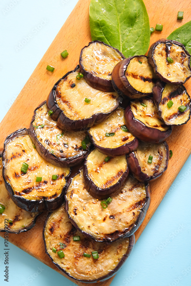 Board with delicious grilled eggplants on light blue background