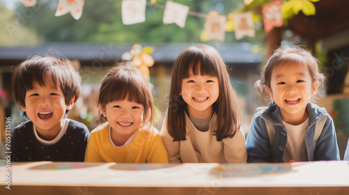 日本の幼稚園児・小学生4人が私服で横に並んで笑っている写真、背景自然の森とガーランド、森のようちえん