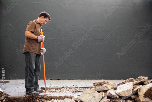 man standing with gloves and a orange crowbar in his hands working construction with gloves and safety goggles