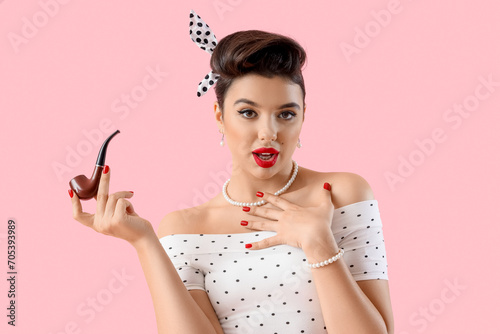 Young pin-up woman with smoking pipe on pink background photo