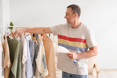 Mature man with steamer and clothes rack at home