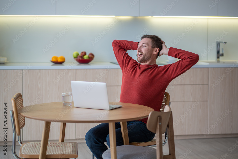 Positive carefree man freelancer, IT programmer, developer, sales manager, working with notebook at home, sitting, resting, straightening back after successful job ending, genius idea realization Positive carefree man freelancer, IT programmer, developer, sales manager, working with notebook at home, sitting, resting, straightening back after successful job ending, genius idea realization