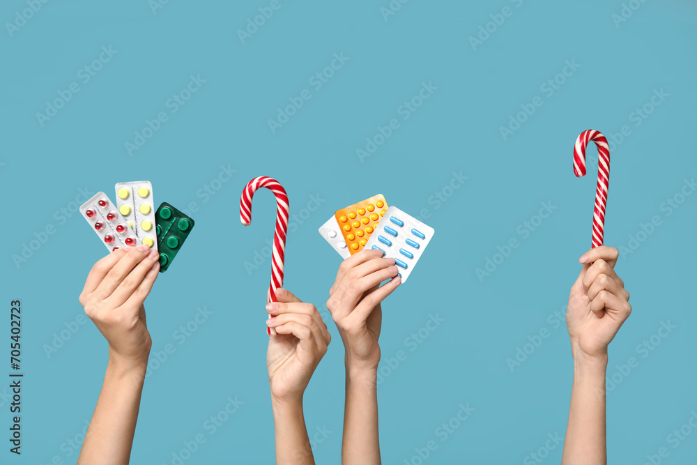 Female hands holding pills in blister packs and candy canes on blue background - obrazy, fototapety, plakaty 