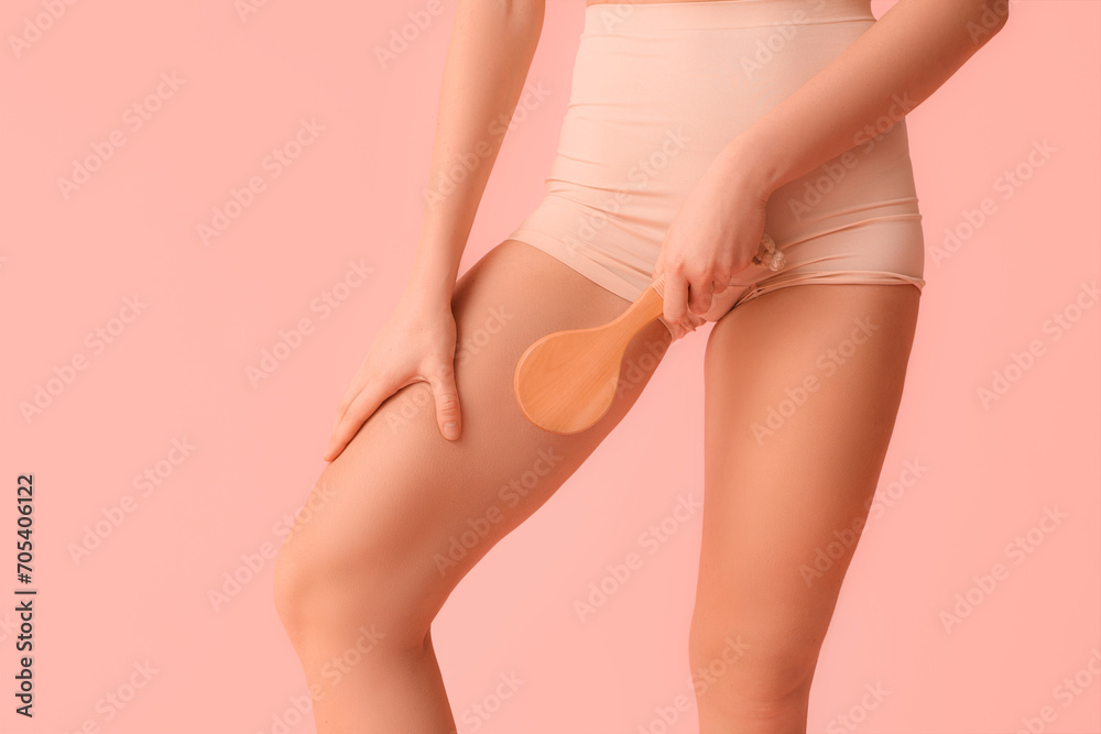 Beautiful young woman with cellulite problem and massage brush on pink background