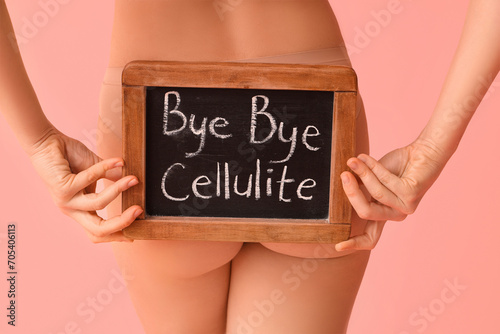 Beautiful young woman holding board with text BYE BYE CELLULITE on pink background, back view