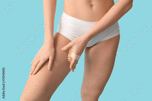 Beautiful young woman with cellulite problem and massage brush on blue background