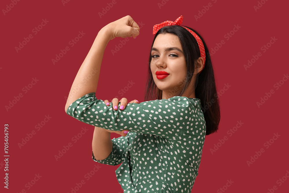Beautiful young happy pin-up woman showing muscles on red background
