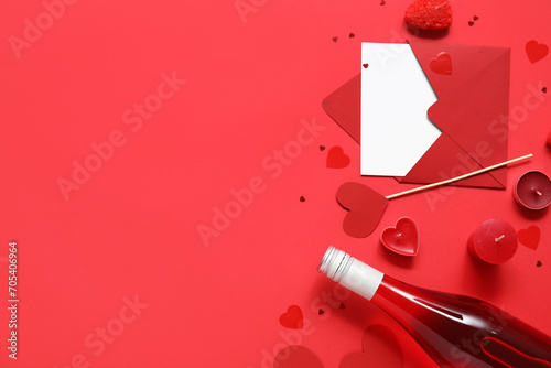 Bottle of wine with paper hearts, candles and envelope on red background. Valentine's Day celebration
