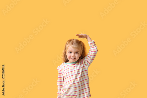 Cute little girl measuring height on yellow background