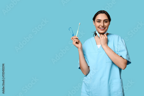 Young female dentist with toothbrush and tongue scraper on blue background photo