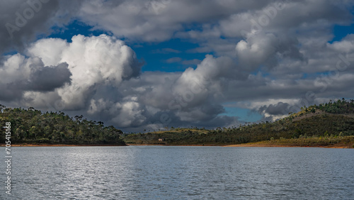 A calm and beautiful lake. Ripples on the water. There is a forest growing on the hilly shores. Picturesque cumulus clouds in the blue sky. Madagascar. Mantasoa Lake. photo