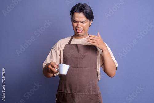 Young barista man holding a cup of coffee and feeling disappointed after tasting bad coffee