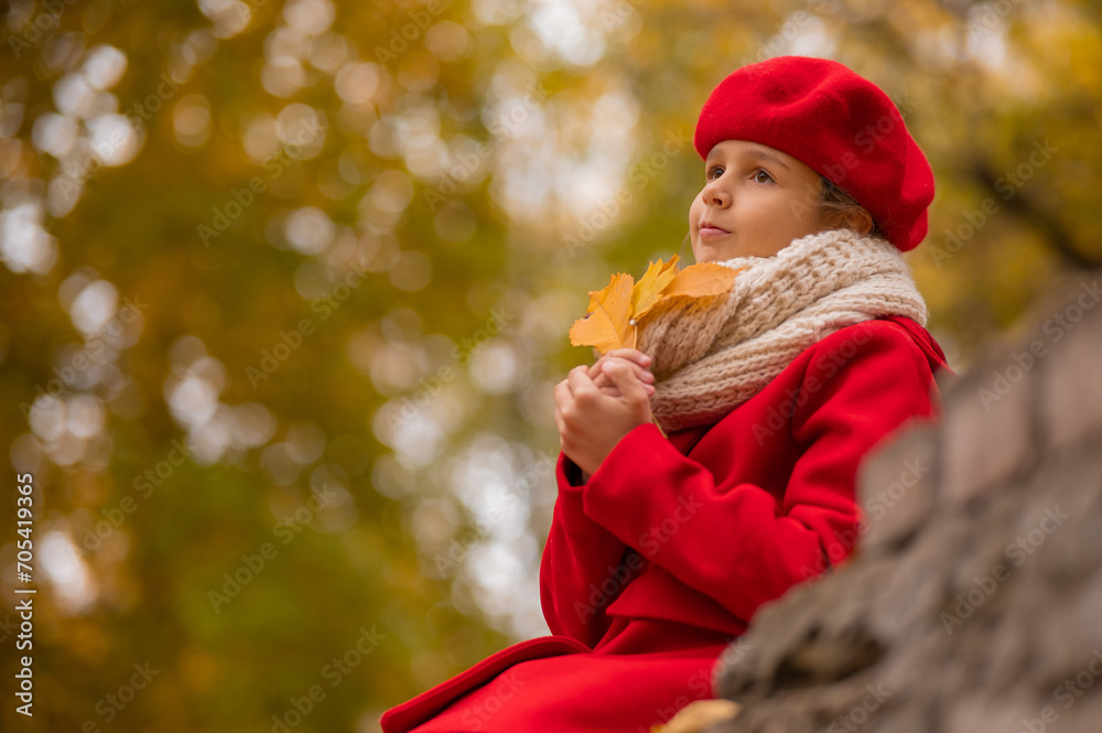 Smiling caucasian girl in a red coat and beret sits on a brick wall on a walk in autumn. Smiling caucasian girl in a red coat and beret sits on a brick wall on a walk in autumn.