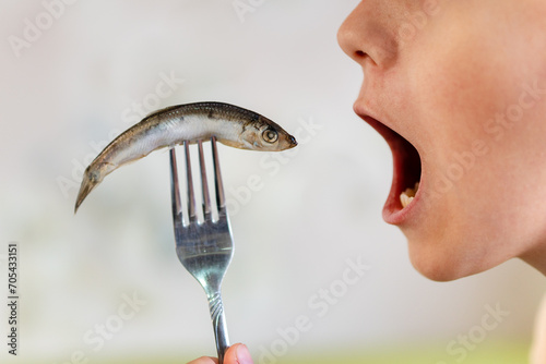sprat in the hands, salty and fresh on white background. open mouth is eating fish. photo