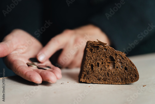 A handout of bread for the poor. the concept of poverty and hunger. Hands of senior woman with bread and coins on wooden background. Poverty concept