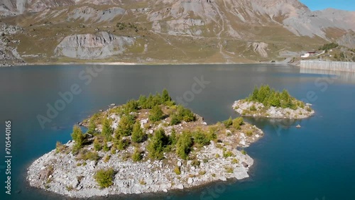 Aerial flyover over an island in the waters of Lac de Salanfe in Valais, Switzerland on a sunny autumn day in the Swiss Alps with a view of surrounding alpine peaks, cliffs and hydroelectric dam. photo