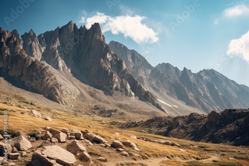 A breathtaking view of a majestic rocky mountain range stretches across the horizon, with lush green grass and rugged rocks in the foreground., A rugged mountain range under a clear sky, AI Generated