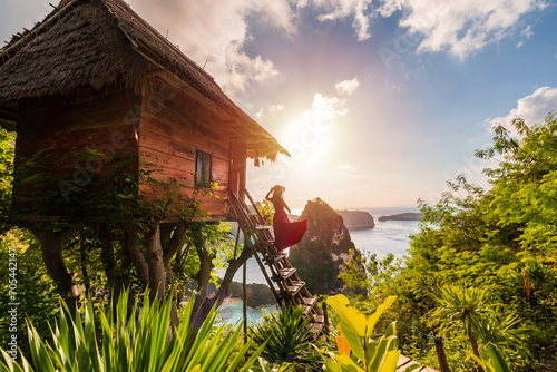 Young woman traveler enjoying and looking beautiful sunrise at the tree house in Nusa Penida island Bali, Indonesia photo