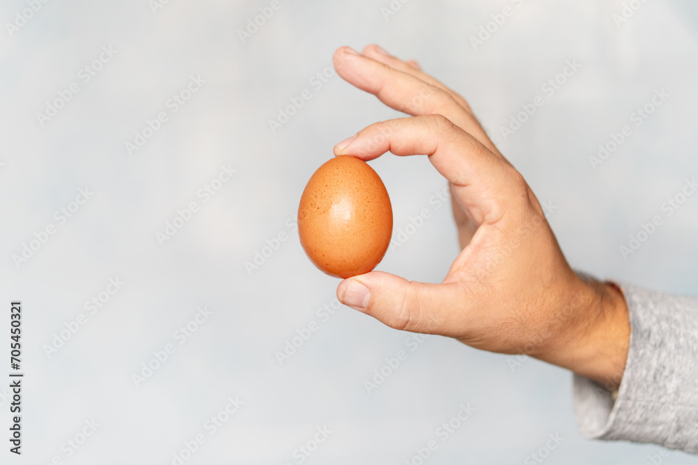 Young hispanic hand holding raw egg over blue background. Young hispanic hand holding raw egg over blue background.