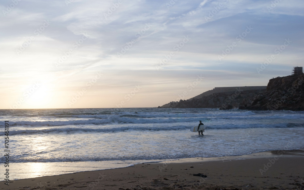 Surfer on the seashore on the beach in Melieha. Sunset in Golden Bay Malta.