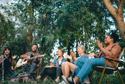 Group of man and woman friends and family singing and playing guitar during having breakfast together. People enjoy and fun outdoor lifestyle travel nature camping on summer holiday vacation. © chokniti