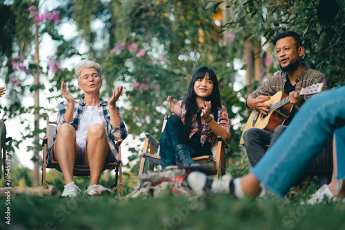 Group of man and woman friends and family singing and playing guitar during having breakfast together. People enjoy and fun outdoor lifestyle travel nature camping on summer holiday vacation. © chokniti