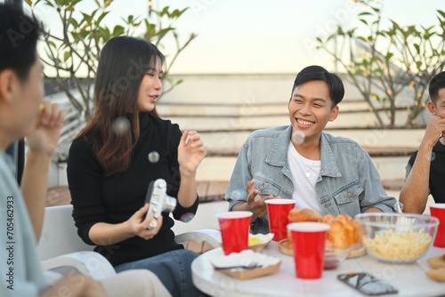 Group of young friends spending great time together chatting and drinking beer at rooftop party