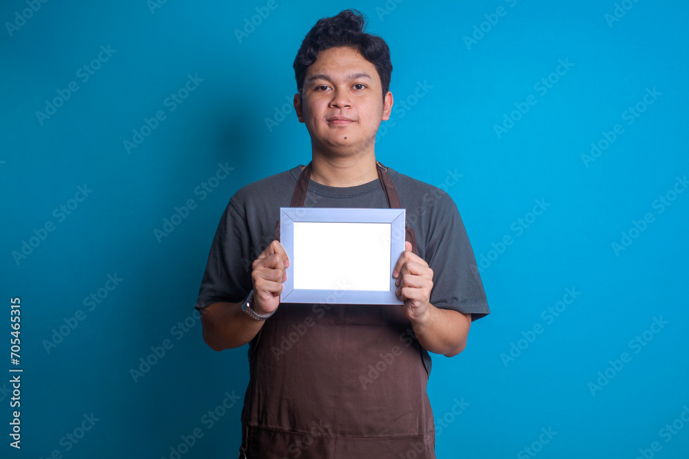 Asian barista or waiter holding a blank white signage for mockup over blue background. Asian barista or waiter holding a blank white signage for mockup over blue background.