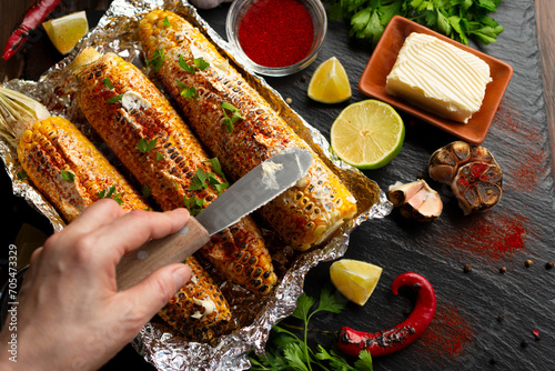 Grilled Sweetcorn with smoked paprika lime and butter on kitchen table being seasoned with table knife flat lay view