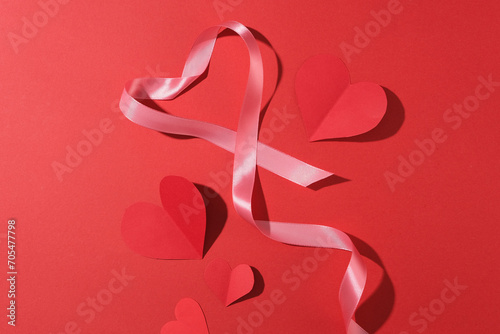 Top view of red paper hearts and pink ribbon decorated on a red background. Saint Valentine, mother's day, birthday greeting cards, invitation, celebration concept